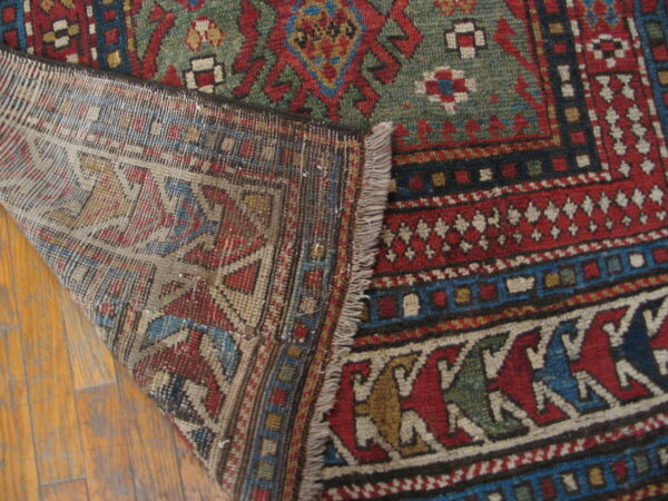 A corner of a traditional red, green, and blue geometric rug is folded over, revealing the woven backing on wood floors.