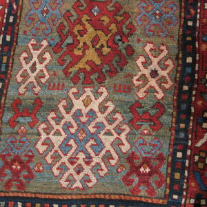 Geometric rug detail showing traditional motifs in red, cream, and gold on a muted teal background.