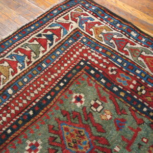 Close-up of a traditional geometric rug in red, green, and blue on distressed hardwood flooring.