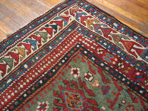 Close-up of a traditional geometric rug in red, green, and blue on distressed hardwood flooring.