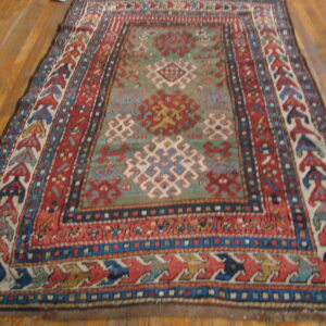 Geometric patterned rug in red, blue, and sage green rests on light brown wooden plank flooring.