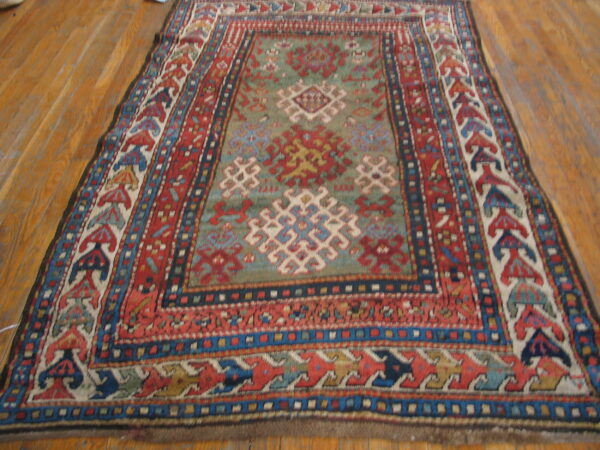Geometric patterned rug in red, blue, and sage green rests on light brown wooden plank flooring.