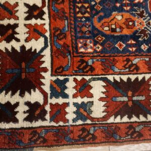 Close-up of a rug corner featuring a navy blue field, rust-red borders, and ivory geometric motifs.