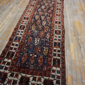 A low pile blue and red geometric runner rug is placed over light-colored rustic hardwood floors.