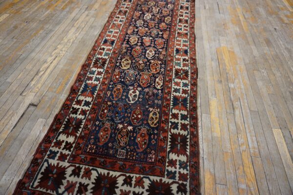 A low pile blue and red geometric runner rug is placed over light-colored rustic hardwood floors.