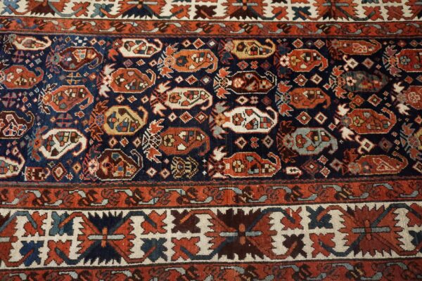 Detailed view of a woven rug in navy blue, rust red, and cream with complex geometric and stylized motifs.
