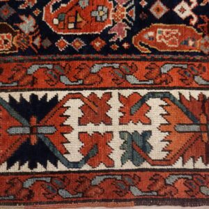 Textured rug detail showing navy blue, rust red, and cream borders with stylized floral shapes.