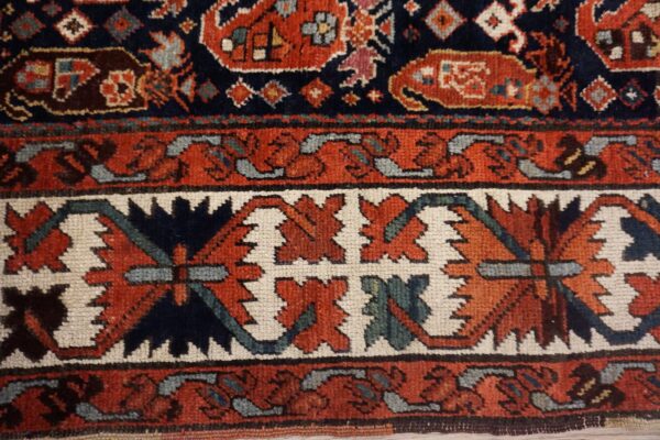 Textured rug detail showing navy blue, rust red, and cream borders with stylized floral shapes.