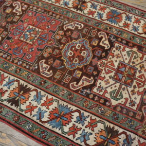 Geometric rug featuring red, brown, blue, and cream borders rests on light wood planks.