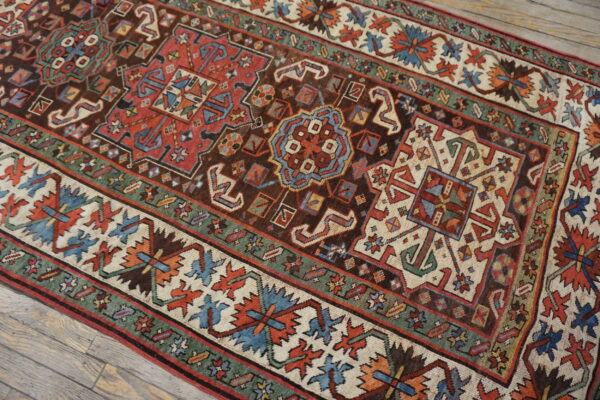 Geometric rug featuring red, brown, blue, and cream borders rests on light wood planks.