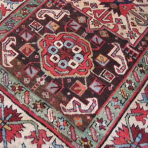 Detailed geometric rug pattern in deep brown, vibrant red, teal, and light cream colors.