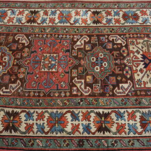 Close-up of a rug featuring geometric tribal motifs on a dark brown field with blue, red, and ivory borders.