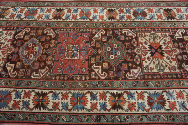 Close-up of a rug featuring geometric tribal motifs on a dark brown field with blue, red, and ivory borders.