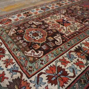 Ornate patterned rug in dark brown, ivory, rust, and teal green on weathered wood planks.
