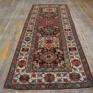 Long traditional runner rug featuring brown, red, cream, and green designs on distressed wood floors.