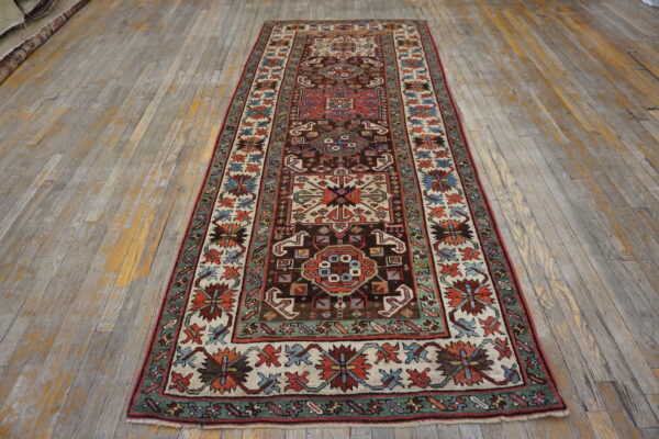 Long traditional runner rug featuring brown, red, cream, and green designs on distressed wood floors.