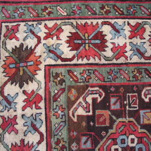 Detailed view of a low pile rug featuring red, blue, green, and brown traditional geometric and floral borders.