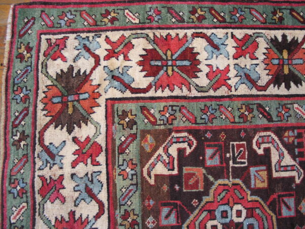 Detailed view of a low pile rug featuring red, blue, green, and brown traditional geometric and floral borders.