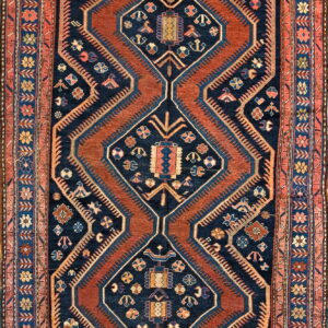 Traditional rug with a navy and rust geometric pattern featuring stacked medallions and a floral border.