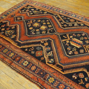 Low-pile geometric rug featuring dark blue, rust, and gold traditional motifs on light hardwood planks.