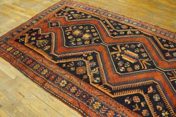 Low-pile geometric rug featuring dark blue, rust, and gold traditional motifs on light hardwood planks.