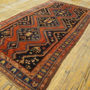 Rust and navy geometric rug featuring stepped diamond patterns rests on worn wood flooring.