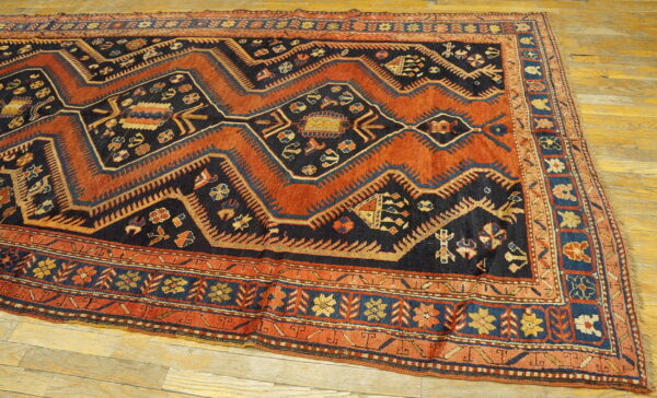 Geometric pattern rug featuring deep rust and navy blue colors, laid on light hardwood flooring.