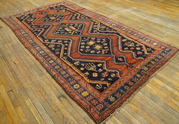 Rectangular navy and rust rug with stepped geometric medallions and patterned borders on wood floor.