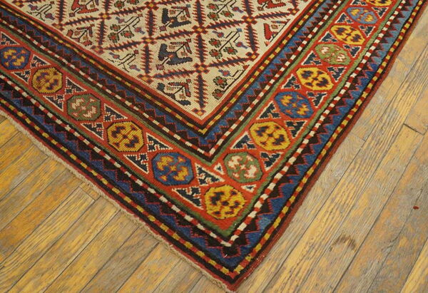 Low pile rug corner displaying a multicolored geometric medallion border and stylized field motifs on distressed wood.