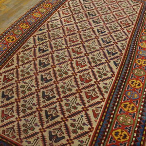 Low-pile rug with a cream field, repeating diamond pattern, and vibrant red, yellow, and blue geometric borders on wood.