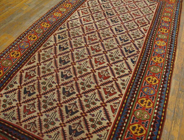 Low-pile rug with a cream field, repeating diamond pattern, and vibrant red, yellow, and blue geometric borders on wood.