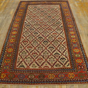Multicolor geometric rug featuring bird and flower motifs on a cream field over worn hardwood.