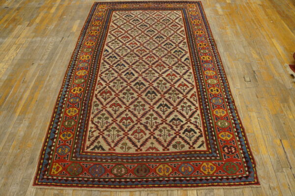 Multicolor geometric rug featuring bird and flower motifs on a cream field over worn hardwood.