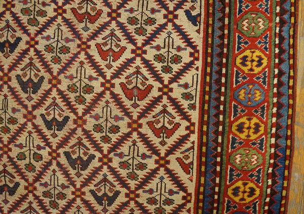 Beige rug field featuring red and blue stylized bird motifs and a thick colorful border with medallions.