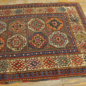 Red, blue, and cream geometric medallion rug with complex borders sits on distressed wood flooring.