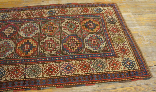 Red, blue, and cream geometric medallion rug with complex borders sits on distressed wood flooring.
