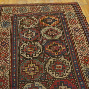Low-pile rug with geometric medallions in muted red, navy, and cream on a light honey wood floor.