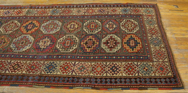 Geometric rug with large red, blue, and beige medallions lying on honey-toned wooden plank flooring.