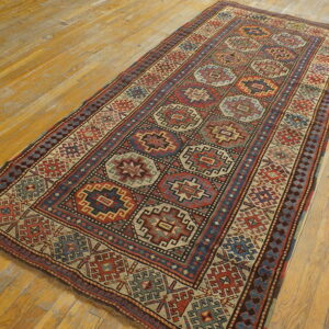 Geometric runner rug in red, navy, and cream patterns on a distressed golden wood floor.