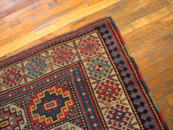 Geometric red, blue, and tan patterned rug lies diagonally on light brown wooden plank flooring.