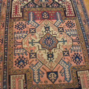 Pink and navy geometric rug with complex central medallions rests on light wood flooring.