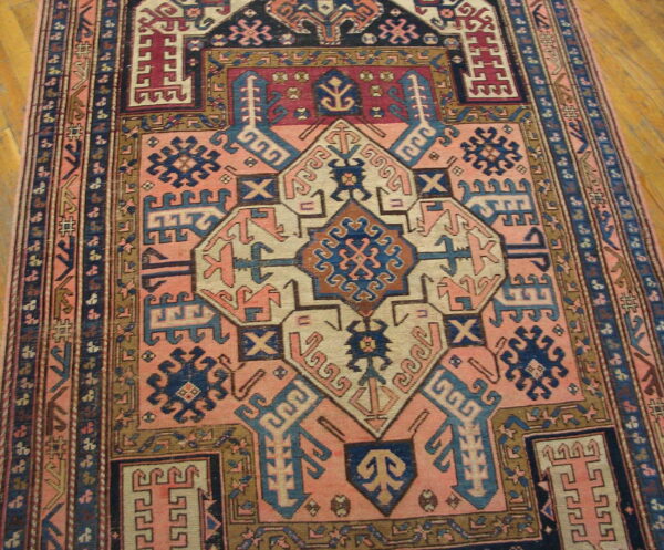 Pink and navy geometric rug with complex central medallions rests on light wood flooring.