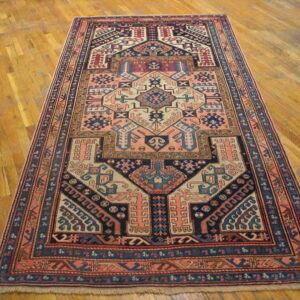 Geometric tribal rug featuring salmon, navy, and cream patterns displayed on light brown hardwood flooring.