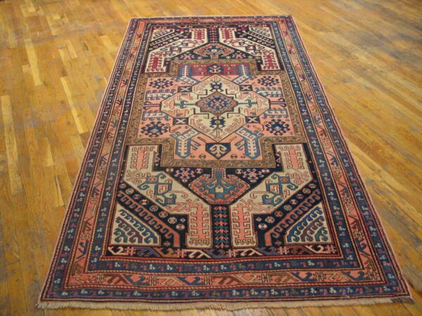 Geometric tribal rug featuring salmon, navy, and cream patterns displayed on light brown hardwood flooring.