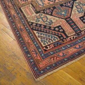 Low pile rug with complex salmon, navy, and blue geometric motifs on worn wooden floor.