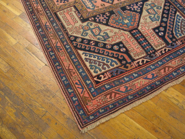 Low pile rug with complex salmon, navy, and blue geometric motifs on worn wooden floor.