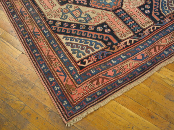 Navy, pink, and tan geometric rug corner shown on warm, distressed wood plank flooring.