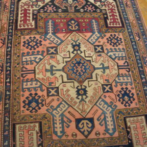 Muted pink and dark blue geometric rug with a central design shown on natural wood flooring.