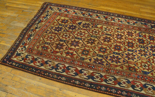 Low-pile rug with geometric star and diamond motifs in red, navy, and tan on wood planks.