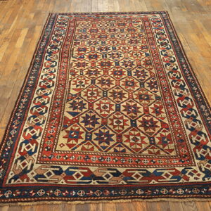 A geometric rug in red, navy, and cream colors lies on wide-plank wood flooring.